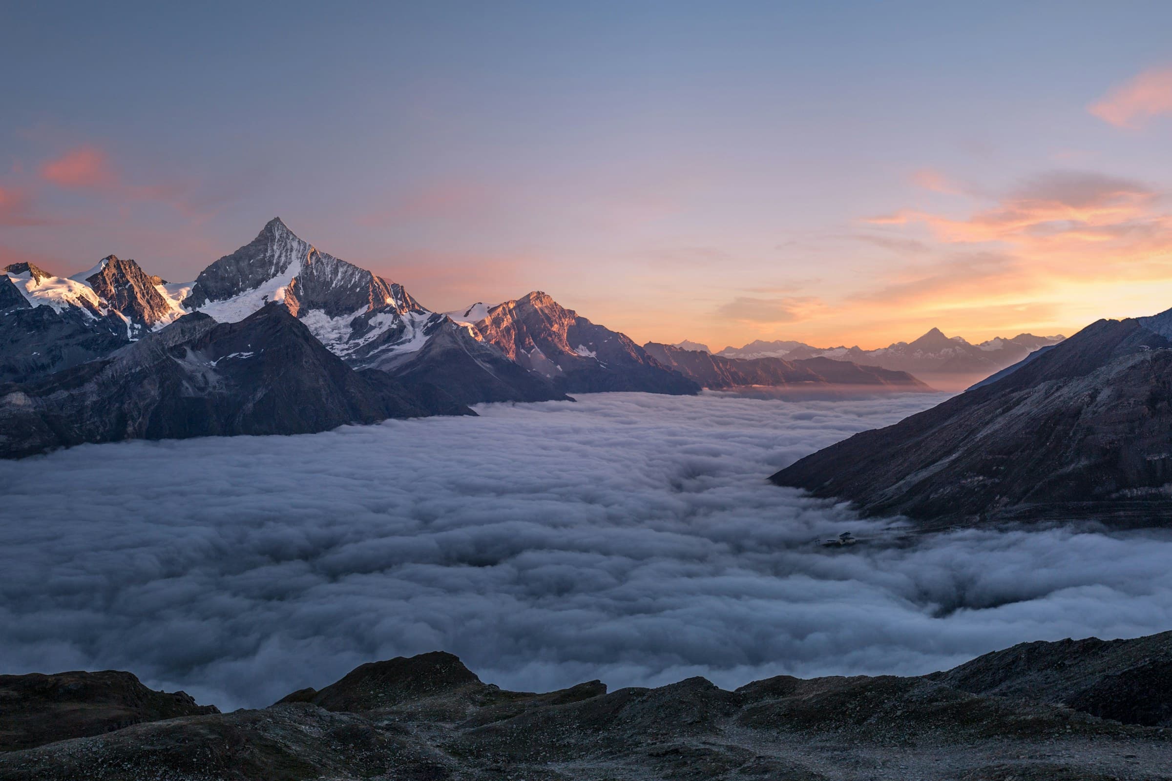 Sommets enneigés des Alpes valaisannes émergeant d'une mer de nuages au crépuscule
